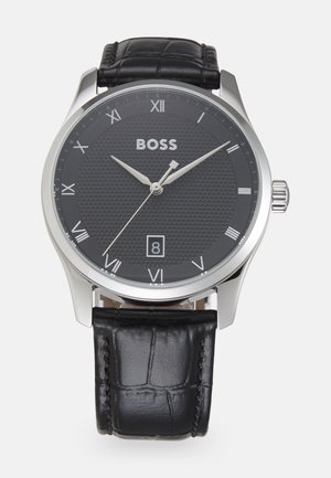 Black leather strap watch with a textured black dial, silver-tone hands, Roman numerals, and date display at 6 o'clock; stainless steel case.
