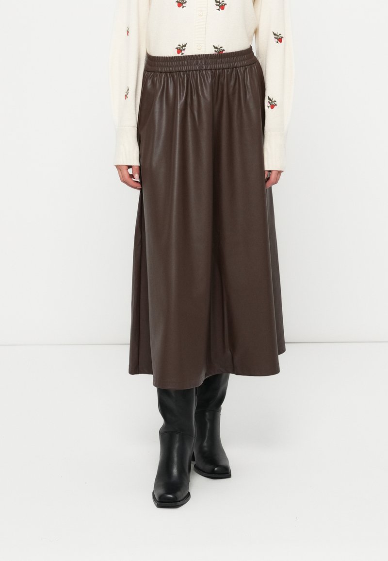 Jupe midi en similicuir marron avec une ceinture élastique, associée à des bottes noires mi-hautes. Le tissu présente une texture lisse et brillante.