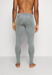 Leggings gris ajustés en matériau extensible, présentant un léger effet satiné, des coutures plates et des accents réfléchissants sur le bas de la jambe.