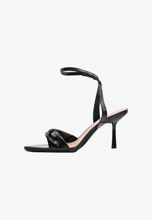 Sandalo nero con tacco alto, sottile cinturino alla caviglia e cinturino attorcigliato sopra le dita, punta aperta e tacco a stiletto stretto.