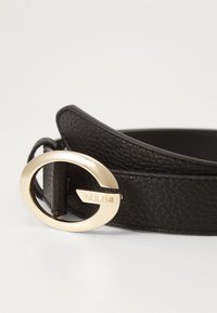 Black leather belt with a textured finish, featuring a round gold-tone buckle with the brand name “GUESS” engraved on it.