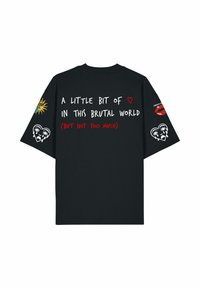 T-shirt noir oversized avec texte blanc et rouge, graphique soleil sur la manche gauche, graphiques de lèvres rouges et cœur qui pleure sur la manche droite.