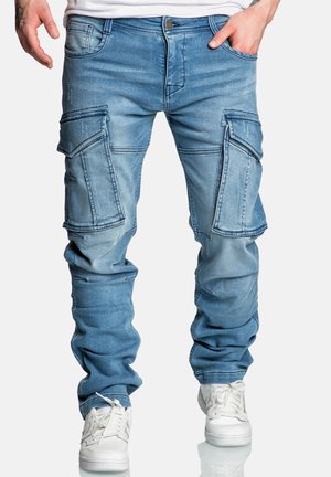 Light blue cargo jeans with multiple pockets, a tapered fit, and distressed texture. Paired with white sneakers for contrast.