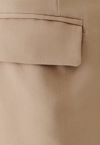 Beige kangas jolla on sileä pinta, jossa on läppätasku, jossa on siisti, räätälöity reuna. Koko suunnittelu on yksinkertainen ja toiminnallinen.