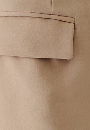 Bēšas krāsas audums ar gludu tekstūru, kas izceļas ar atloku kabatu ar tīru, pielāgotu malu. Kopējais dizains ir vienkāršs un funkcionāls.