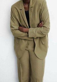Blazer verde oliva e pantaloni abbinati in tessuto morbido. Il blazer presenta una vestibilità morbida, rever a punta e tasche laterali.