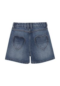 Jeansshorts med elastisk midja, med två hjärtformade fickor på baksidan. Tyget är i ett medelblå tvätt med lätt urtvättning.