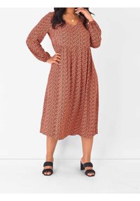Abito a maniche lunghe con scollatura a V, caratterizzato da un motivo floreale arancione e crema su uno sfondo scuro, con una silhouette fluida a forma di A. Indossato con sandali neri con tacco.