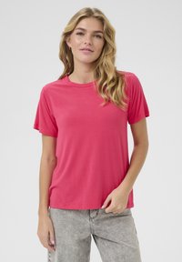 T-shirt rose à manches courtes en tissu lisse, avec un col rond et une coupe décontractée. Assorti à un jean gris clair.