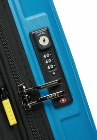 Valigia rigida di un blu vivace con superficie testurizzata, zip nera, lucchetto a combinazione e etichetta gialla Delsey. Accenti in argento.