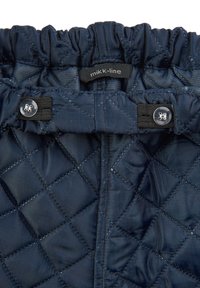 Cinturilla de tela acolchada azul marino con fruncido elástico, correa negra ajustable con botón a presión y una etiqueta con el nombre de la marca "mikk-line".