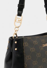 Zwarte leren handtas met gouden hardware, voorzien van een textuur, opvallend logo-patroon en decoratieve studs aan de zijkant.