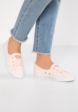 Baskets basses Converse rose clair portées avec un jean bleu clair à ourlet effiloché sur un fond clair.