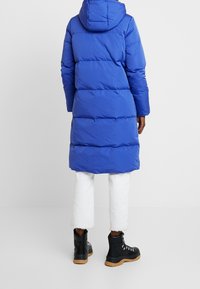 Blue puffer coat with hood, featuring horizontal quilting. Worn over white cropped pants and black lace-up boots with tan soles.