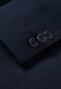 Marineblauw stof met een gladde textuur, voorzien van drie zwarte knopen op een manchetten. De knoopsgaten zijn zichtbaar, wat het op maat gemaakte ontwerpdetail toont.