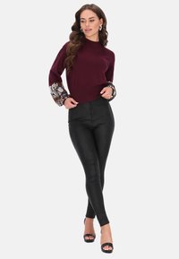 Bordeaux pullover met patroon op de klokmouwen, gecombineerd met zwarte aansluitende broek en strapsandalen. De stof heeft een gladde afwerking.