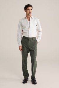 Hvid skjorte med knapper og lange ærmer, kombineret med grønne skræddersyede bukser og sorte loafers. Glat stof og rent design.