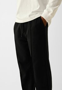 Black sweatpants with a relaxed fit, featuring side pockets and an adjustable drawstring waist. Made of soft fabric with a smooth texture.