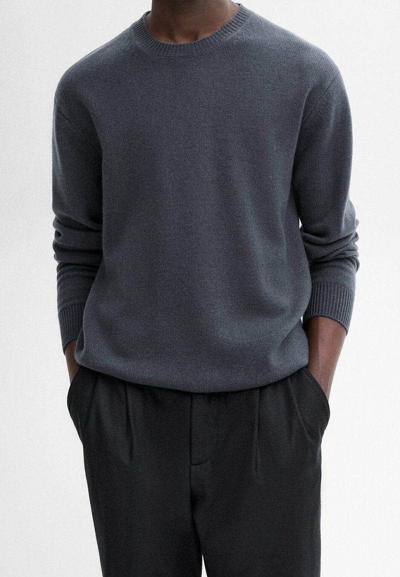 Maglione grigio in morbido tessuto con collo rotondo, maniche lunghe e polsini a costine, abbinato a pantaloni neri. Design minimalista senza motivi.