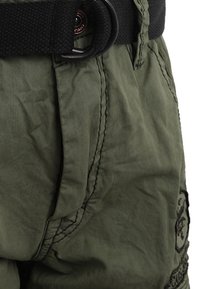 Shorts verde oliva con finitura testurizzata, dotati di una cintura nera passata attraverso un anello di metallo e cuciture dettagliate lungo le cuciture.