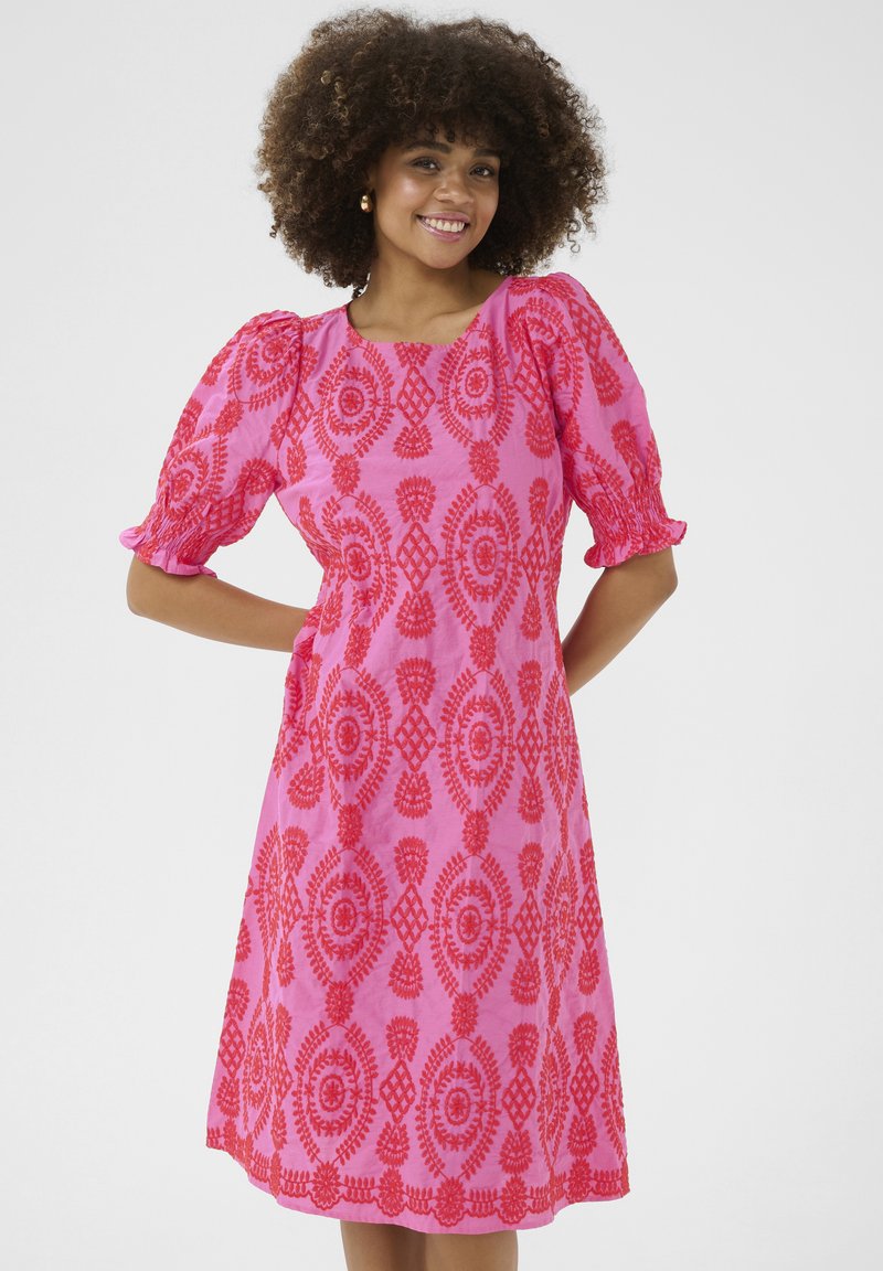 Roza obleka z napihnjenimi rokavi, s kompleksnimi rdečimi vzorci in valovitim robom. Narejena iz lahkotnega materiala za sproščen kroj.