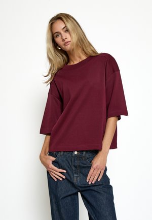Camiseta oversize burdeos de manga corta, con un escote redondo y fabricada en algodón suave y liso. Combinada con vaqueros azul oscuro.