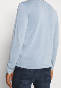 Hellblaues Langarm-Sweatshirt aus Baumwollmischung mit Rundhalsausschnitt und gerippten Bündchen, kombiniert mit dunkelblauen Jeans.