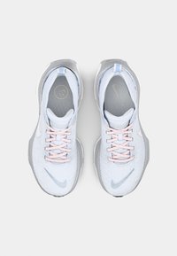 Baskets Nike bleu clair avec un tissu texturé, des accents gris, des lacets roses et une semelle lisse. Comprend un logo près du talon.