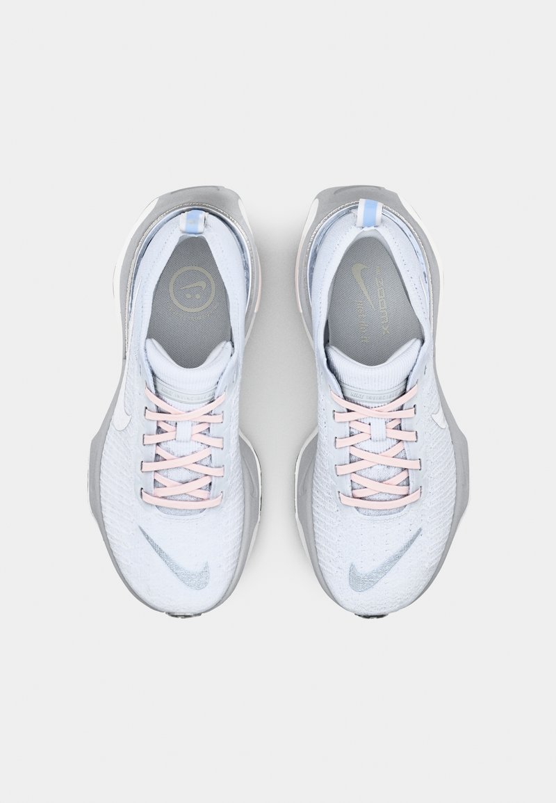 Sneakers Nike di colore blu chiaro con tessuto texturizzato, dettagli grigi, lacci rosa e suola liscia. Include un logo vicino al tallone.