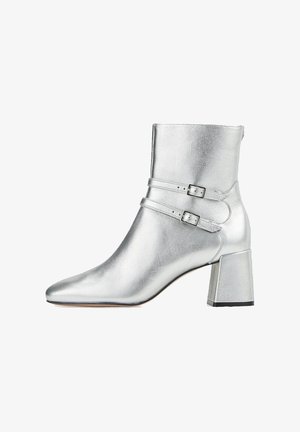 Bottine argentée en cuir métallisé, dotée d'un bout pointu, de deux brides ajustables avec boucles, et d'un talon rectangulaire à bloc.