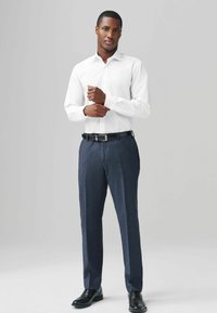 Chemise blanche à col, associée à un pantalon taillé bleu foncé et des chaussures en cuir noires. Design minimaliste avec une texture lisse.