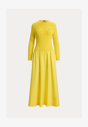 Żółta dzianinowa sukienka z kabelkowym wzorem na górze i długimi rękawami, przechodząca w marszczony, rozkloszowany dół. Na piersi małe logo.