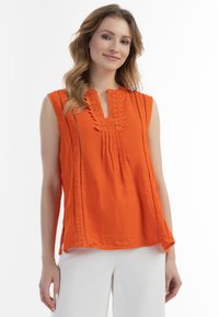 Lys orange ærmeløs bluse med en klippet krave, teksturerede detaljer og lodrette sømme. Letvægtsstof med afslappet pasform.