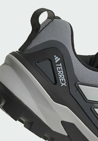 Sneaker grigia con tomaia texturizzata, dettagli neri, tallone rinforzato e il marchio "TERREX" in evidenza. Suola in gomma spessa con battistrada robusto.