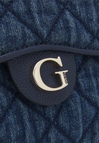 Czarna torba z denimu pikowanego, z niebieską skórzaną klapą o teksturze i metalicznym złotym akcentem w kształcie logo 'G'.