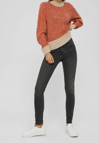 Texturerad orange-röd tröja med en beige ribbad nederkant, matchad med svarta skinny jeans och vita sneakers. Outfiten har en avslappnad passform.