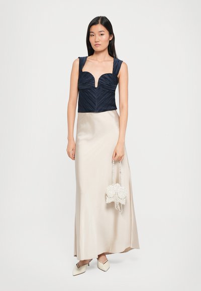 Tumes pleated crop top südamekujulise kaelusega, millele on sobitatud kreemjas satiinist maxi-seelik ja pärlitega käekott. Valged moolid lõpetavad looki.