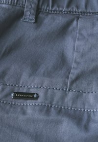 Tessuto grigio con una superficie liscia, caratterizzato da una cucitura orizzontale e un piccolo etichetta metallica con la scritta "Street One" cucita lungo il fondo.