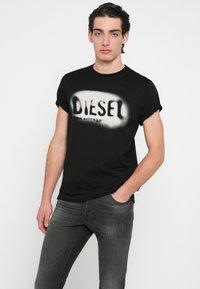 Čierne bavlnené tričko s jemne natretým bielym logom "DIESEL" na hrudi, krátkymi rukávmi a okrúhlym výstrihom.