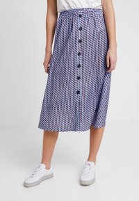 Una gonna lunga fino al ginocchio, decorata con un motivo geometrico blu, rosso e bianco, con bottoni sul davanti e una cintura elastica.