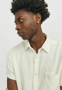Chemise à manches courtes, avec col, de couleur crème clair, ornée d'un motif texturé et dotée d'une poche poitrine. Comprend une patte de boutonnage et un tissu doux.