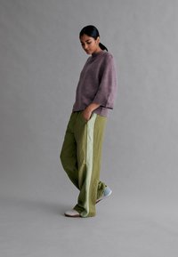 Lilla tekstureret sweater med trekvartærmer, parret med løse olivenfarvede bukser med lys grønne sidelængder og casual sko.