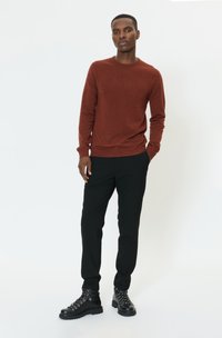 Piros hosszú ujjú pulóver fekete karcsúsított nadrággal és fekete fűzős csizmával párosítva. Sima textúra, testhezálló kialakítás és kontrasztos színek.