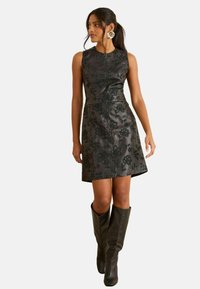 Rochie neagră fără mâneci, cu un design floral în relief, în formă de A, și o textură netedă. Asortată cu cizme negre din piele până la genunchi.