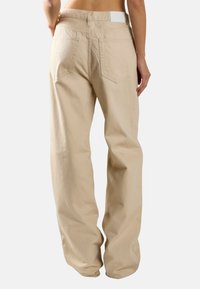 Beige, losse broek van katoen met een gladde textuur. Voorzien van een witte tailleband en twee achterzakken.