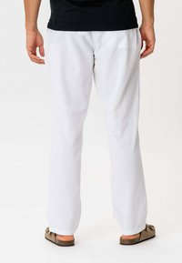 Hvide linnedbukser med en afslappet pasform, der har elastisk talje og manchetter. Båret med brune slidesandaler, der viser en afslappet stil.