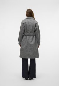 Manteau en laine gris avec une taille ceinturée, grand col et manches longues. Poches à rabat sur les côtés, longueur mi-mollet, finition texturée.