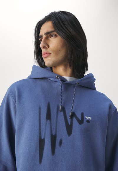 Blå fleecehoodie med dragsko i huvan, med ett tryckt mönster och logotyp på bröstet. Mjuk textur, avslappnad passform.