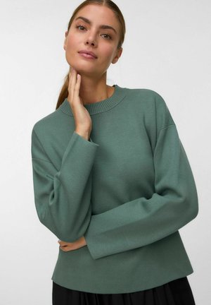 Grüner Strickpullover mit Rundhalsausschnitt, gesenkten Schulternähten und langen Ärmeln. Der Stoff wirkt weich und hat eine strukturierte Oberfläche.