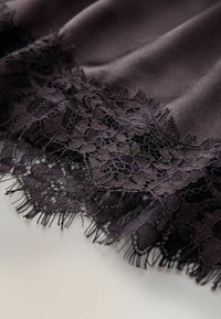 Tessuto nero con bordo in pizzo floreale smerlato, caratterizzato da motivi intricati e una delicata frangia lungo il bordo, disteso su una superficie chiara.